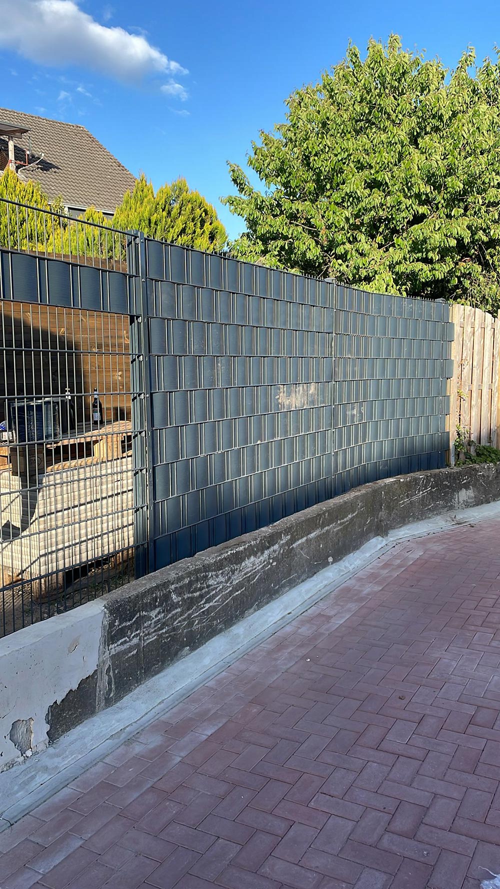 Ein moderner Zaun aus dunklem Metall mit schattigem Bereich und grünen Bäumen