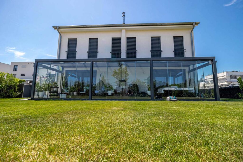 Modernes weißes Haus mit großer verglaster Terrasse und gepflegtem grünen Rasen