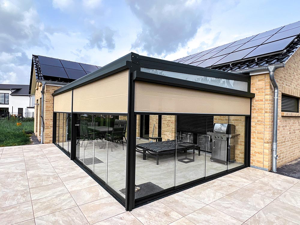 Ein moderner Wintergarten mit Glaswänden und beige Markise steht am Haus mit Solarpanelen