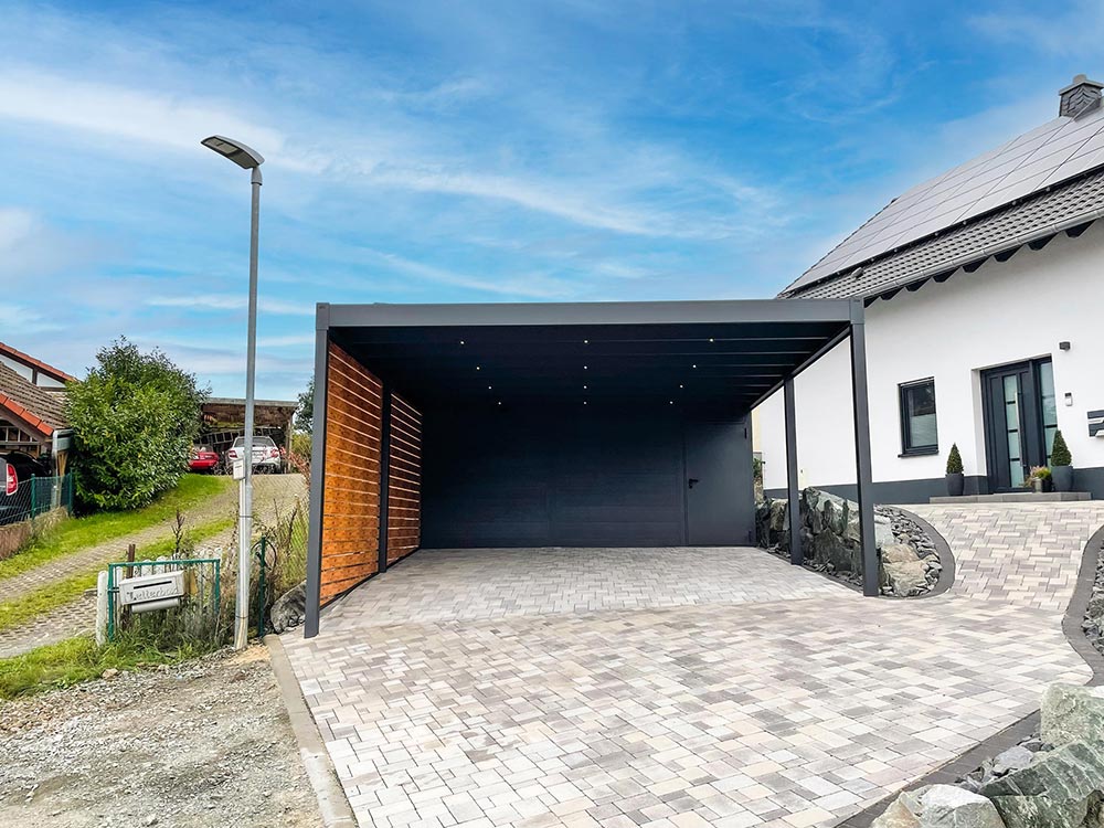 Ein moderner schwarzer Carport mit Holzverkleidung steht neben einem weißen Haus