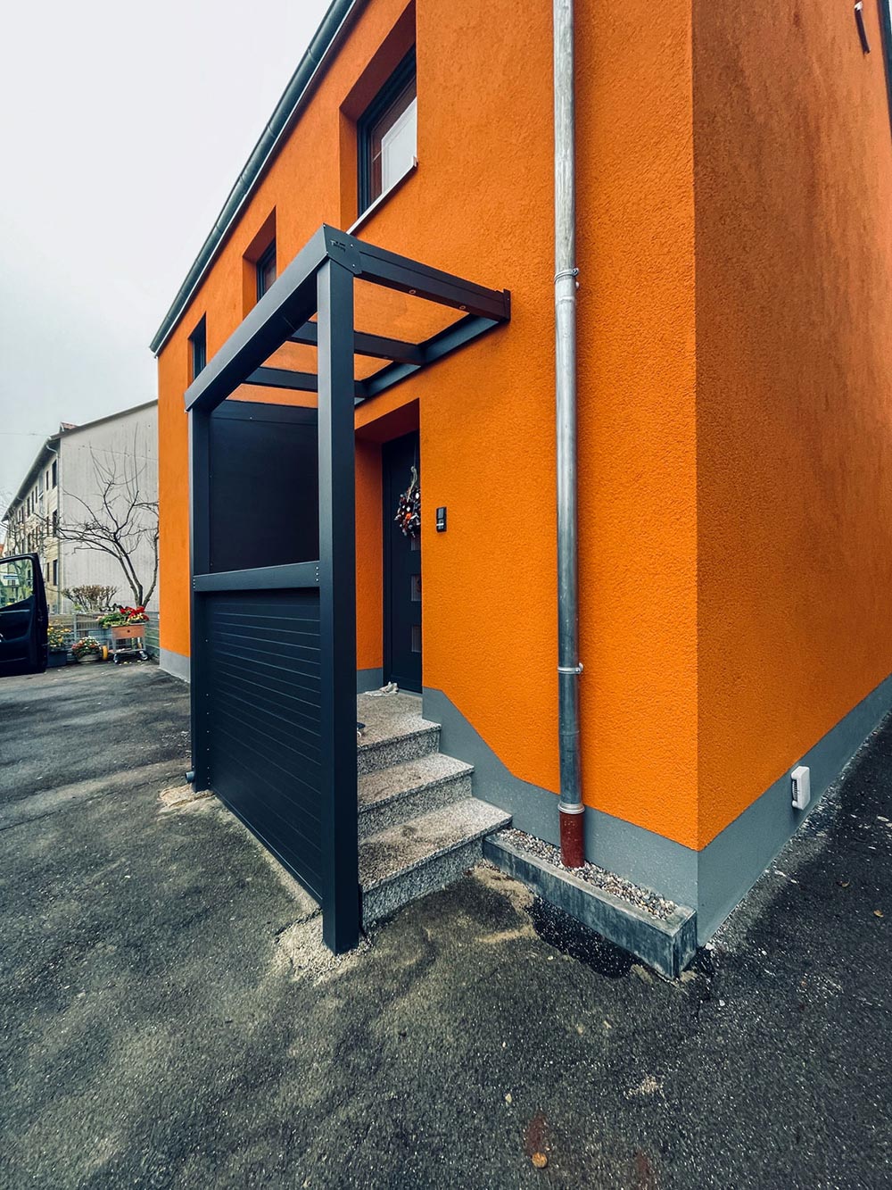 Eine moderne orangefarbene Hausfassade mit grauem Vordach und Stufen am Eingang