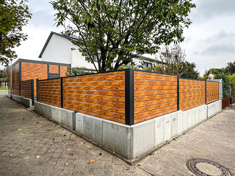 Moderner Garten mit hellbraunem Holzzaun und grauen Betonelementen an einer Straßenecke