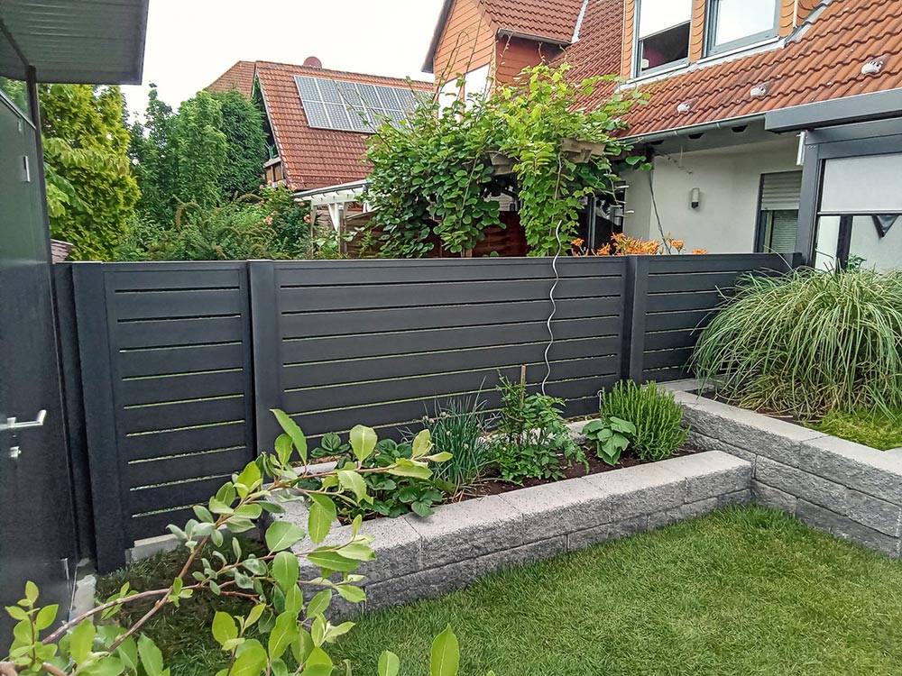Moderner Garten mit grauem Sichtschutzzaun, Hochbeeten und üppigem Grün